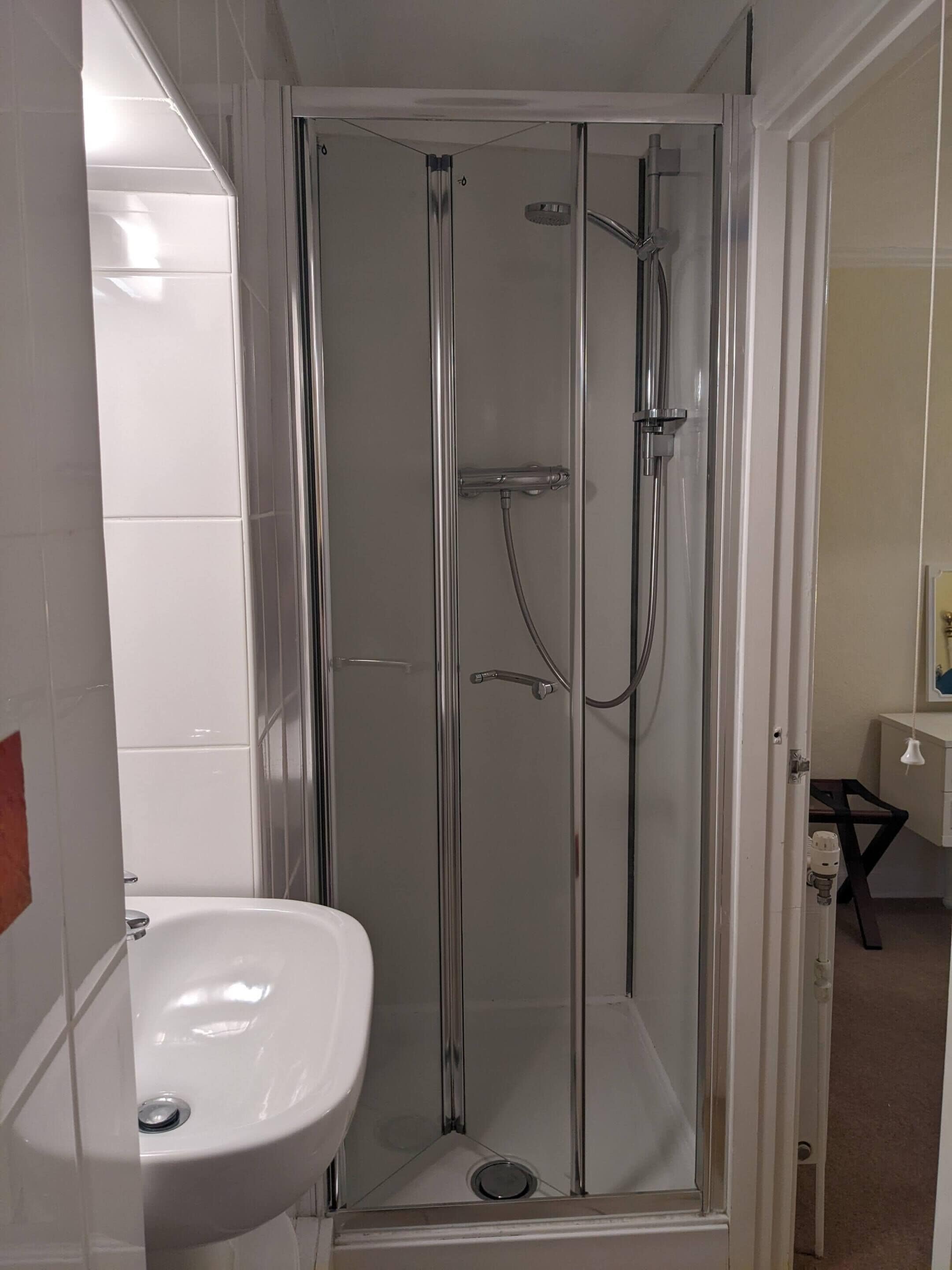 A glass-enclosed shower with a handheld showerhead and a wall-mounted faucet.