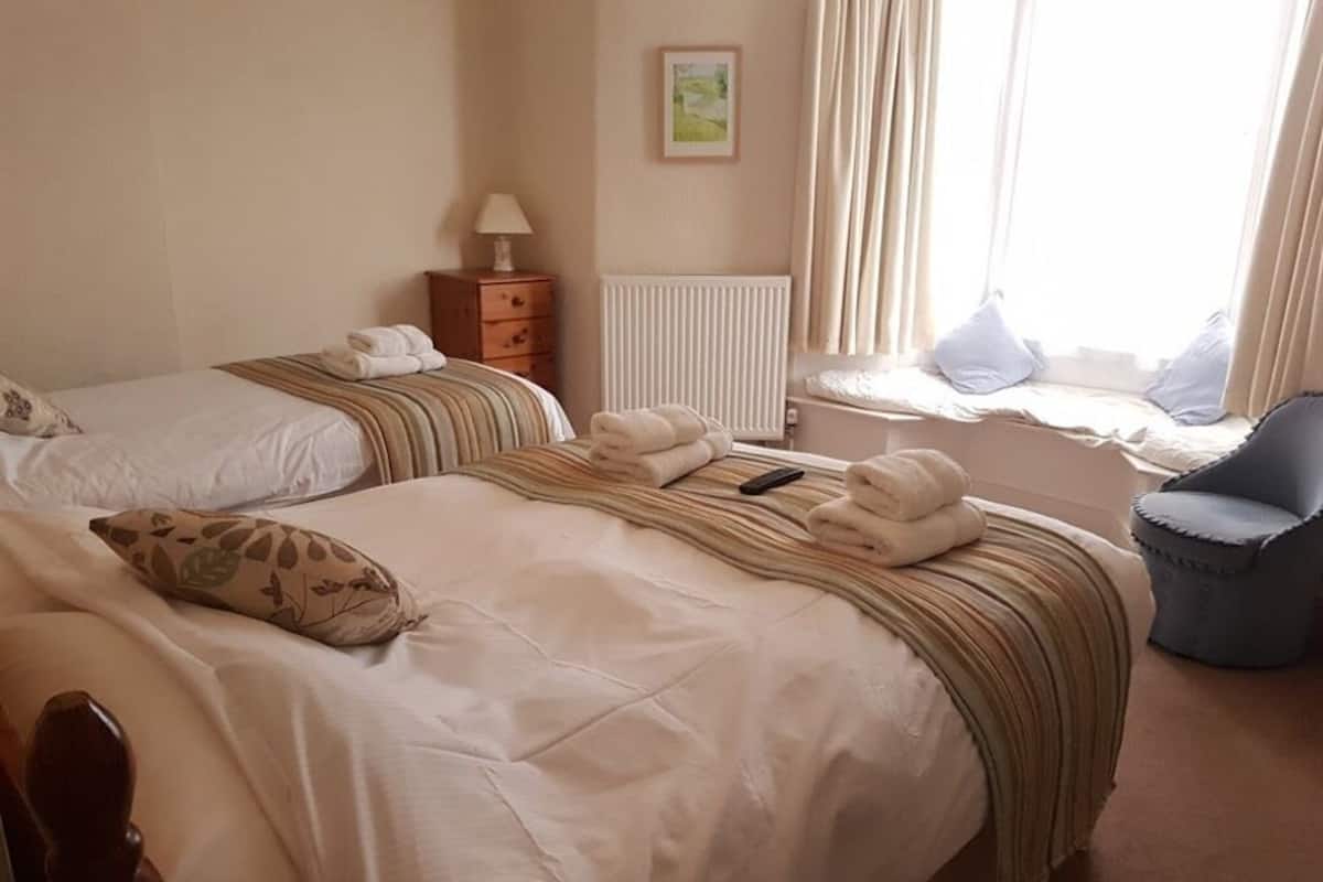 Habitación de hotel con dos camas, una ventana con cortinas, una silla y un radiador.