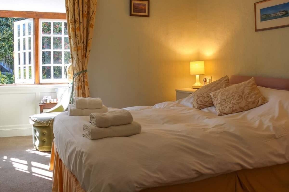 Una cama bien hecha con toallas dobladas, una lámpara de noche y una ventana con cortinas.