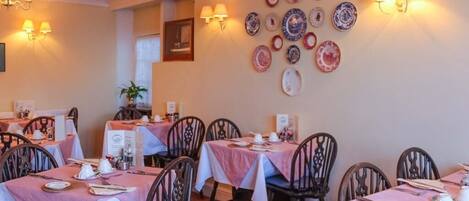 A dining area with tables set for service, chairs, and wall-mounted light fixtures.