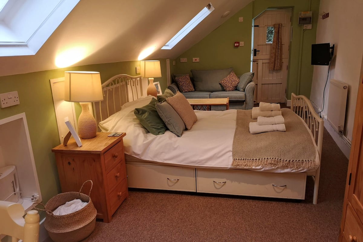 Un dormitorio acogedor con cama, mesita de noche, lámpara y un pequeño cofre de madera.