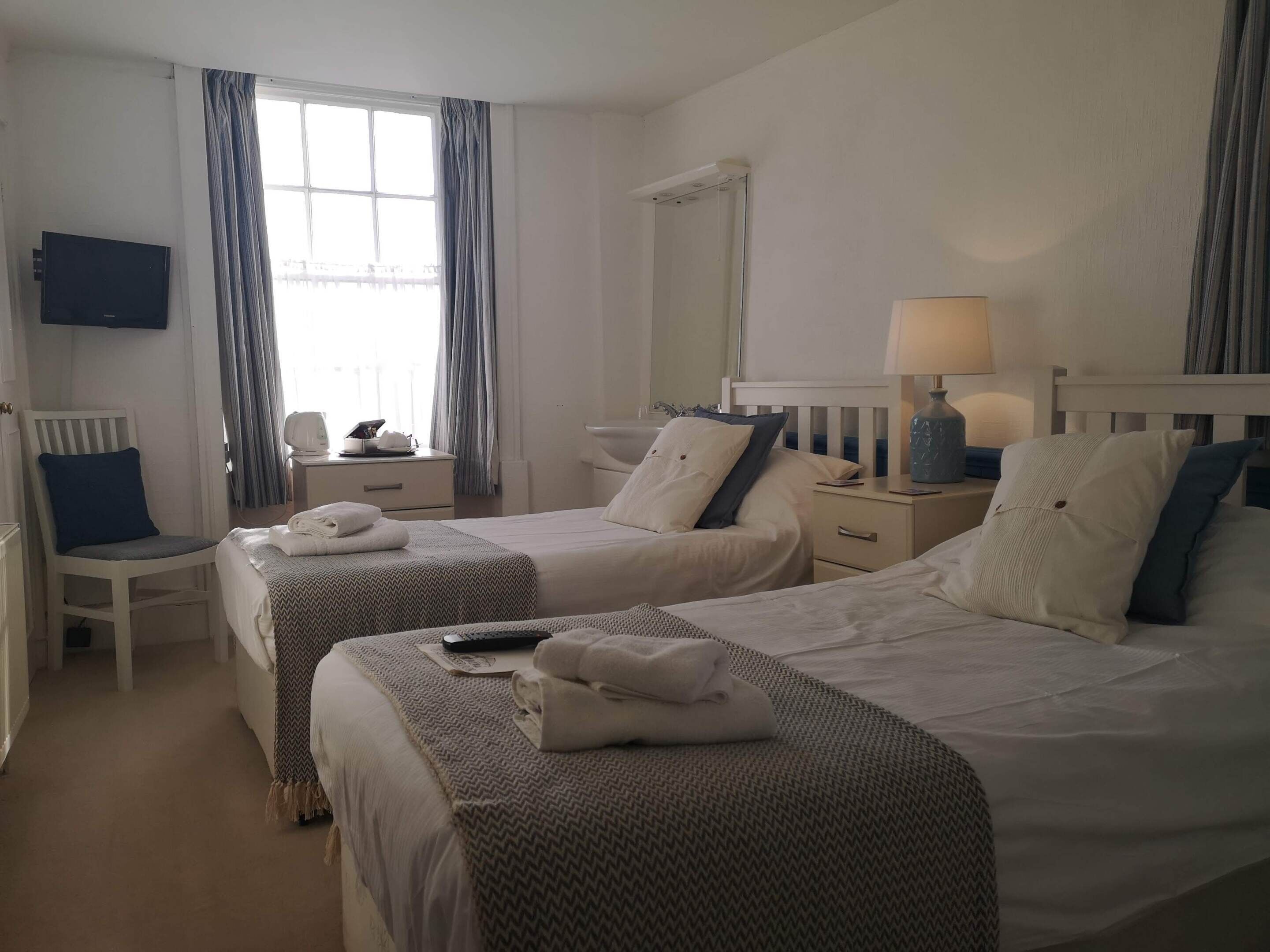 A hotel room with two beds, a desk, a chair, a TV, and a window with curtains.
