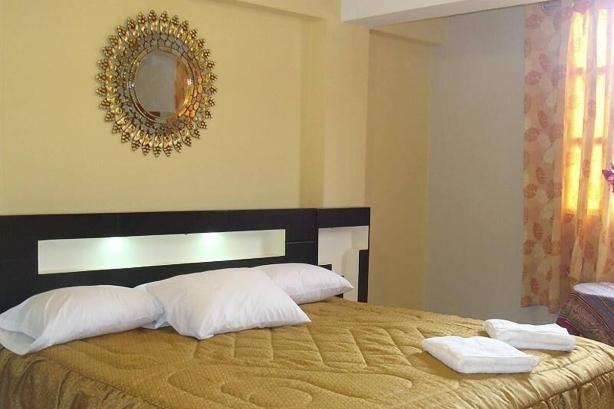 A hotel room with a bed, pillows, a headboard, a mirror, and a window with curtains.