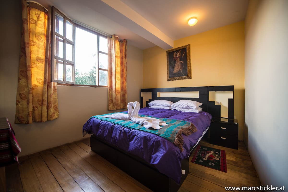 A bedroom with a bed, a nightstand, a window with curtains, and a painting on the wall.