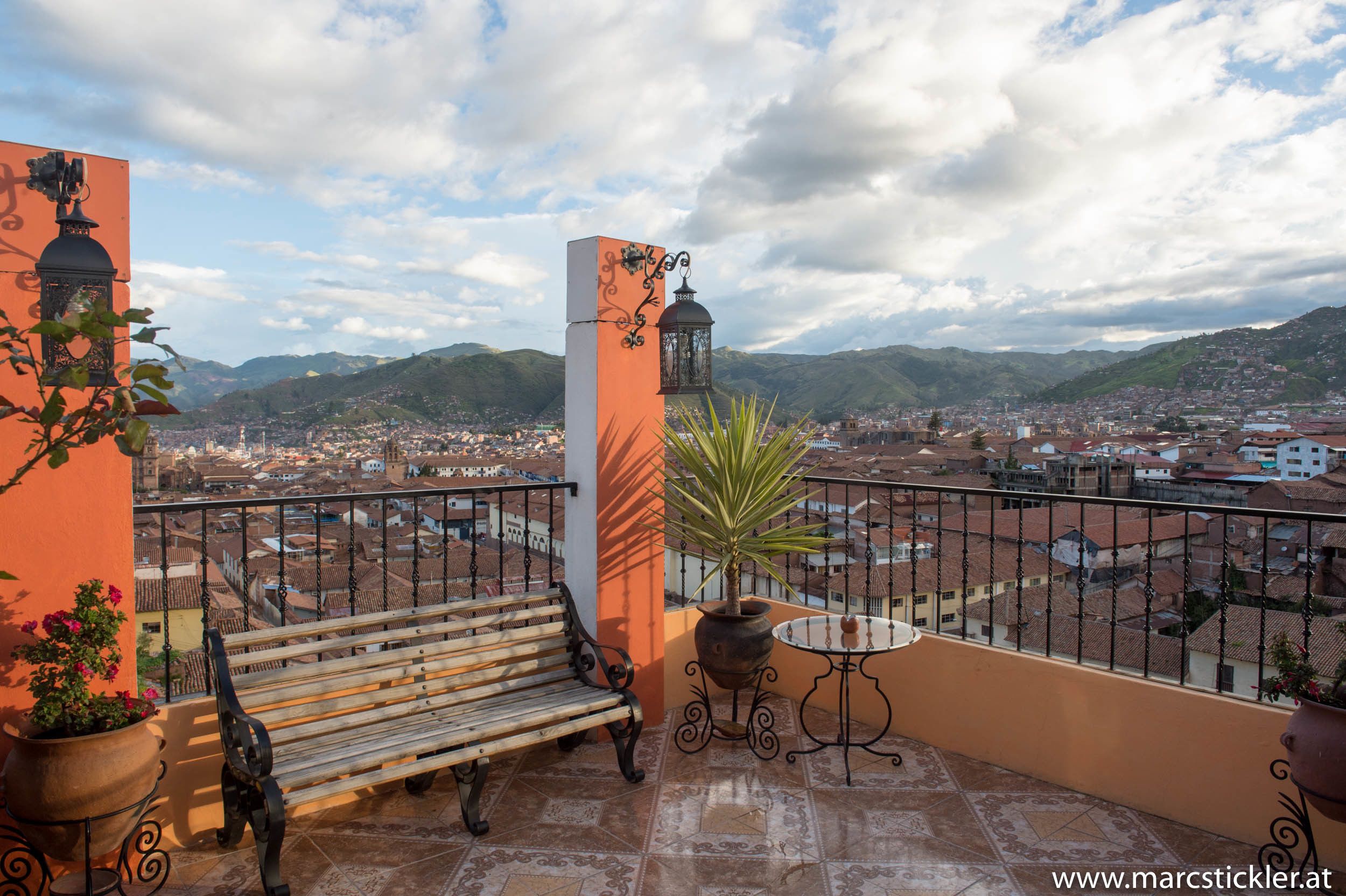 A balcony with a wooden bench, a potted plant, and a table.