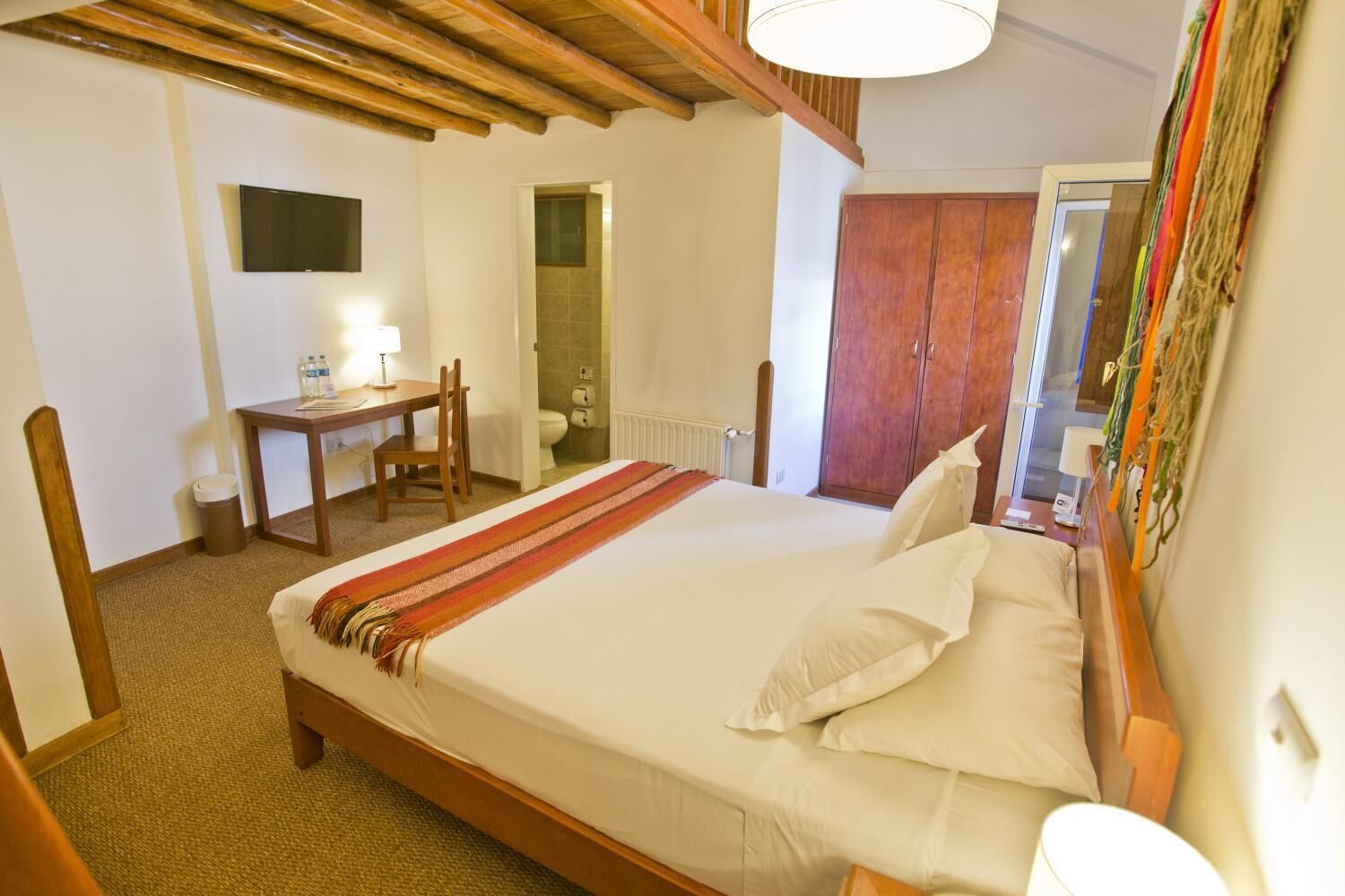 A hotel room with a bed, a desk, a chair, a television, and a wardrobe.