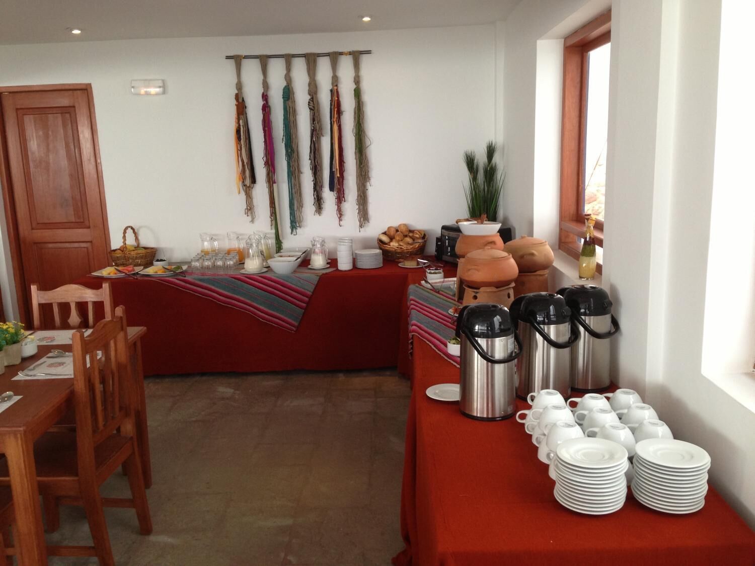 A breakfast setup with a red tablecloth, a variety of breakfast items, and a wall display of colorful fabrics.