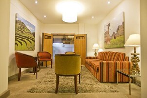 Een woonkamer met een bank, stoelen, een vloerkleed en kunstwerken aan de muur.