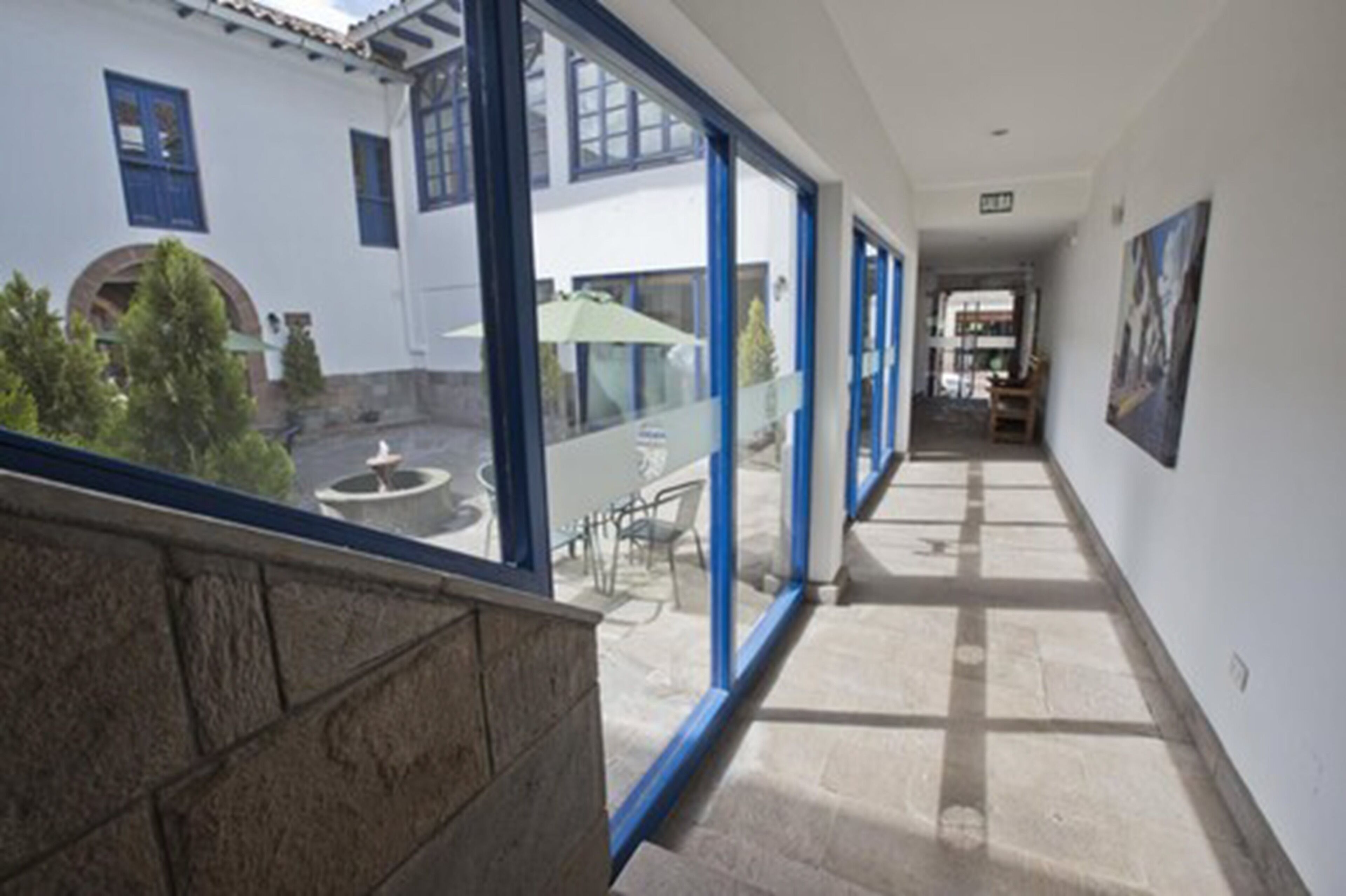 A corridor with large windows, a stone balustrade, and a view of outdoor seating.