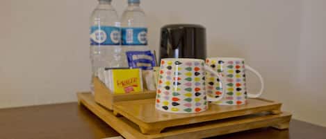 Una bandeja de madera con dos tazas de colores, una botella de agua, un paquete de aperitivos y una termo sobre una mesa.