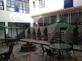 Un'area patio esterna con pavimento in pietra, diversi tavoli e sedie, ombrelloni verdi e piante in vaso.