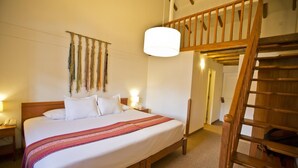 A hotel room with a wooden bed, a red and white striped blanket, a wall hanging, and a wooden staircase. - Tierra Viva Cusco Centro (Cusco)