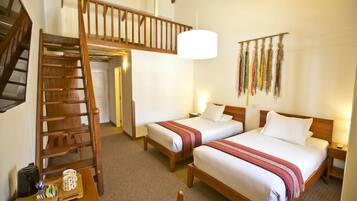 A hotel room with two beds, a wooden staircase, a coffee maker, and a wall-mounted lamp.