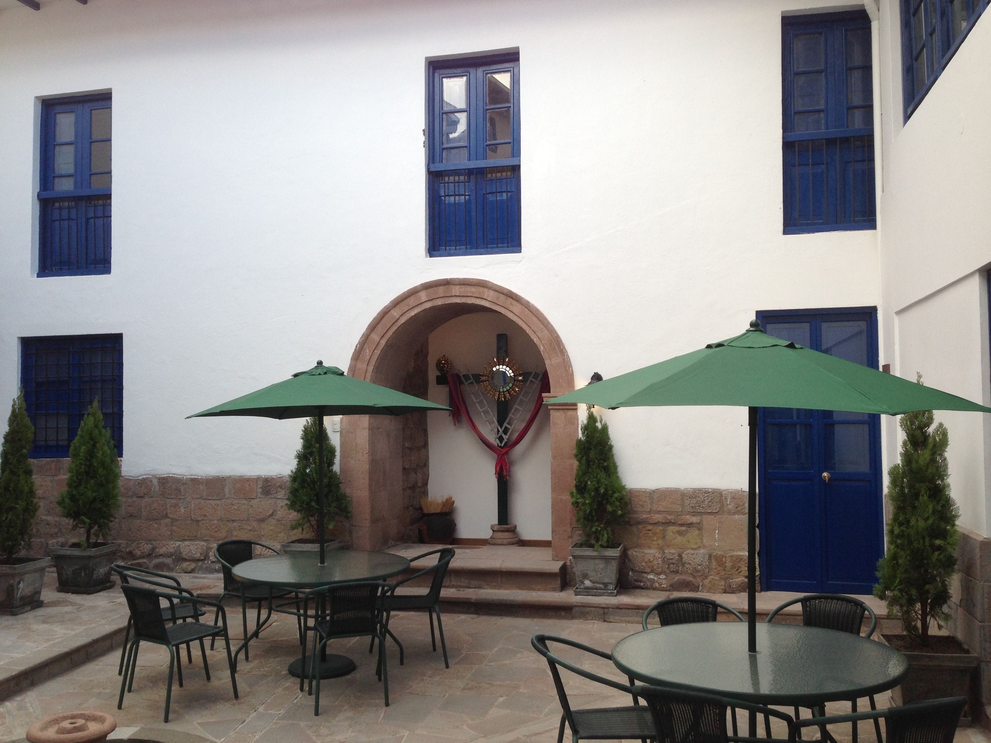 An outdoor patio with round tables and chairs, a green umbrella, and a stone wall.