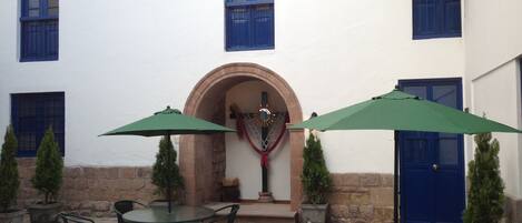 Un patio al aire libre con mesas y sillas redondas, una sombrilla verde y un muro de piedra.