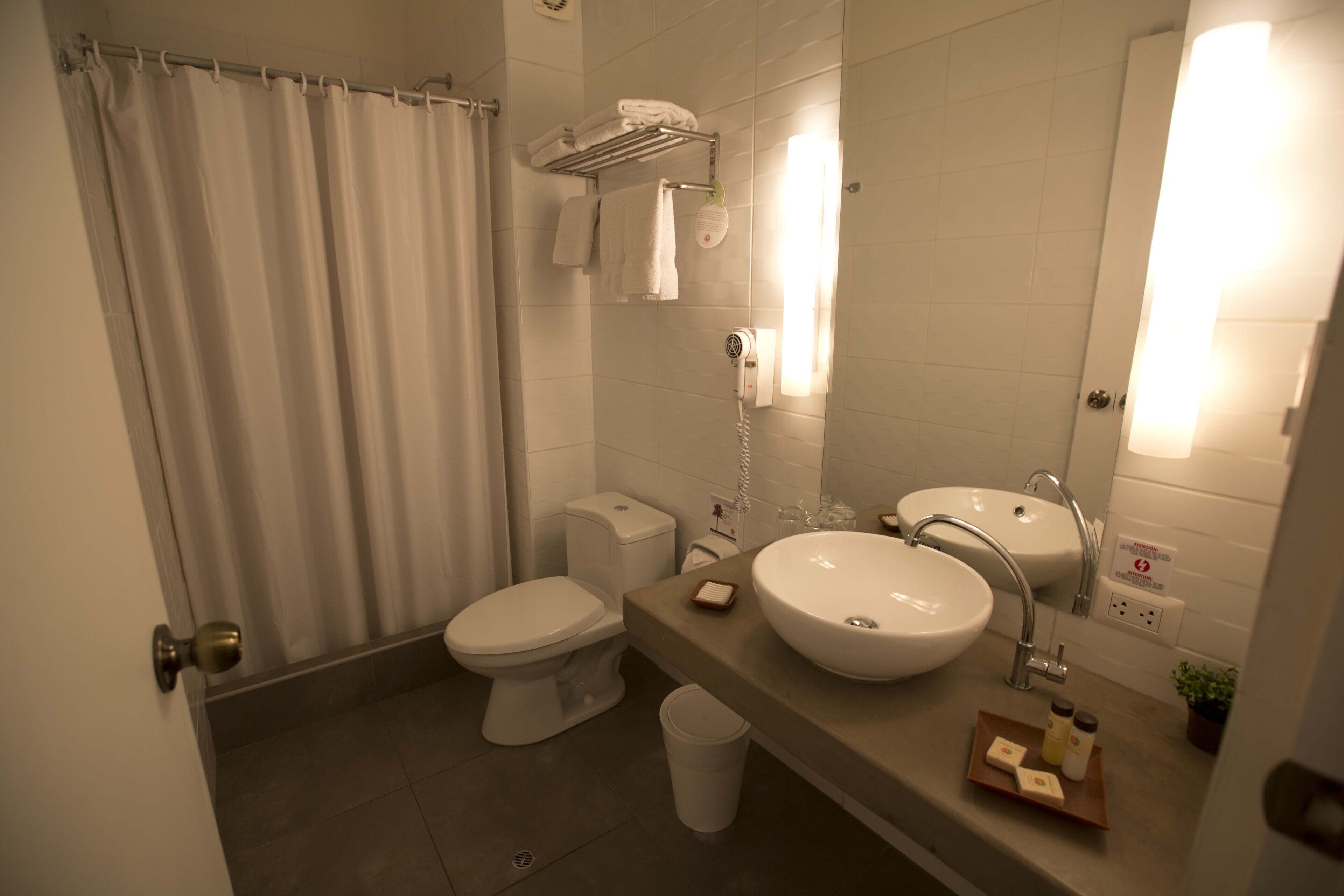 A modern bathroom with a toilet, bidet, sink, and a shower curtain.