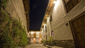 A narrow cobblestone alleyway flanked by buildings with stone walls and wooden doors, leading to a brightly lit entrance. - Tierra Viva Cusco Centro (Cusco)