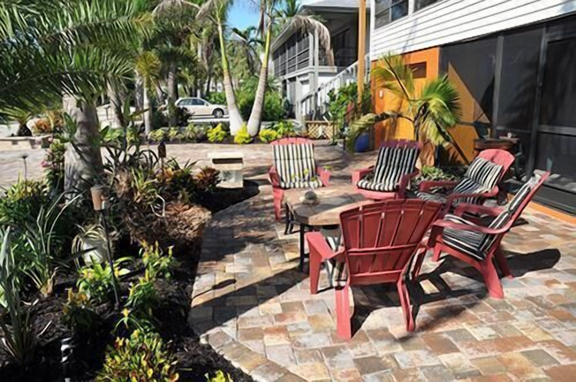 An outdoor seating area with red chairs and a table, surrounded by tropical plants and a stone pathway.