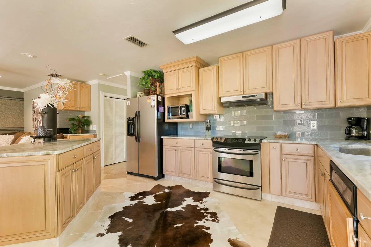 A modern kitchen with light wood cabinets, stainless steel appliances, and a cowhide rug.