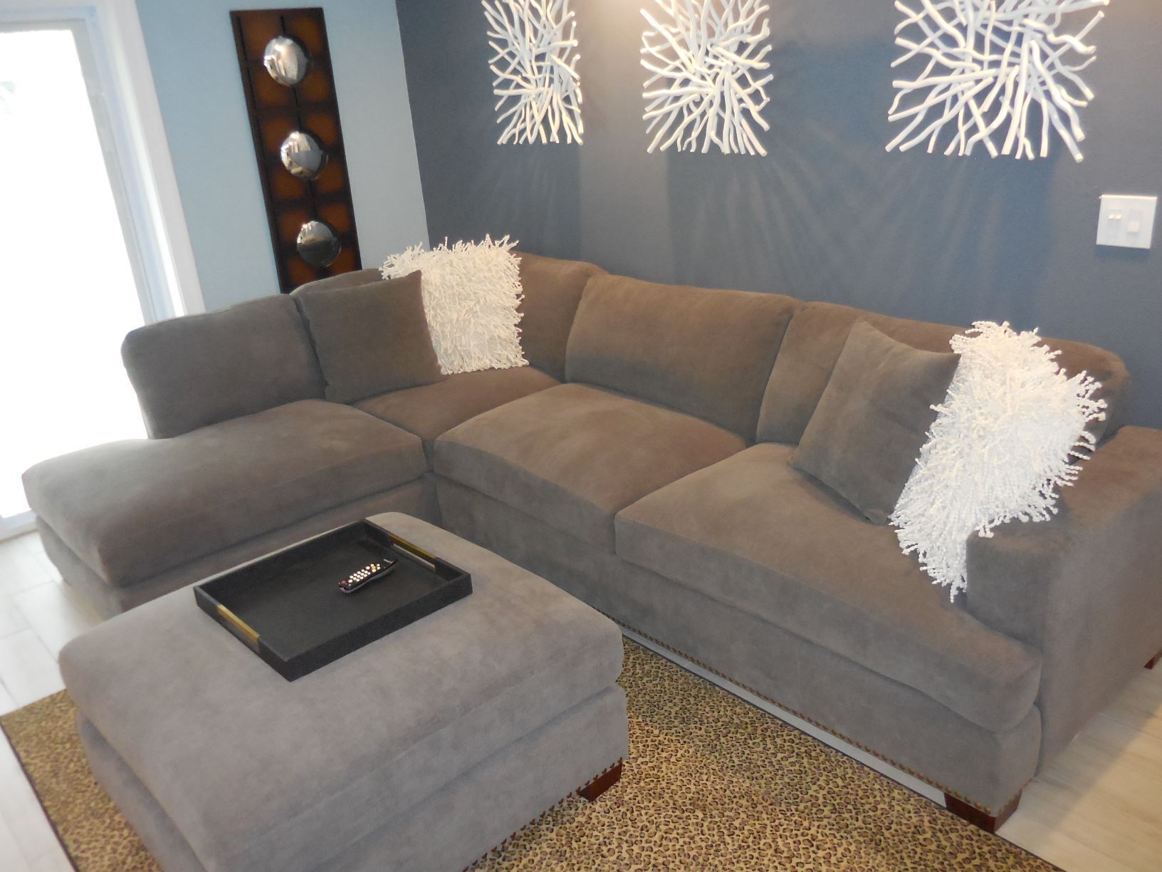 A sectional sofa with white throw pillows, a matching ottoman, and abstract wall art.