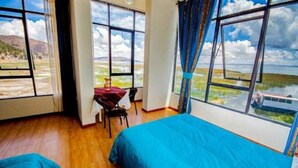 A room with a large bed, a small table, and a chair. There are large windows offering a view of the landscape. - Yacht Lago Titicaca (Puno)