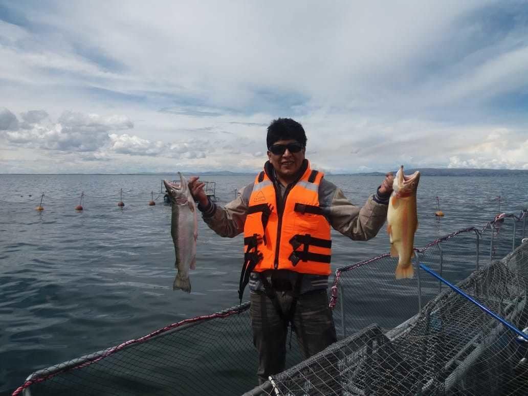 Una persona su una barca tiene in mano dei pesci, con una rete e delle boe nell'acqua.