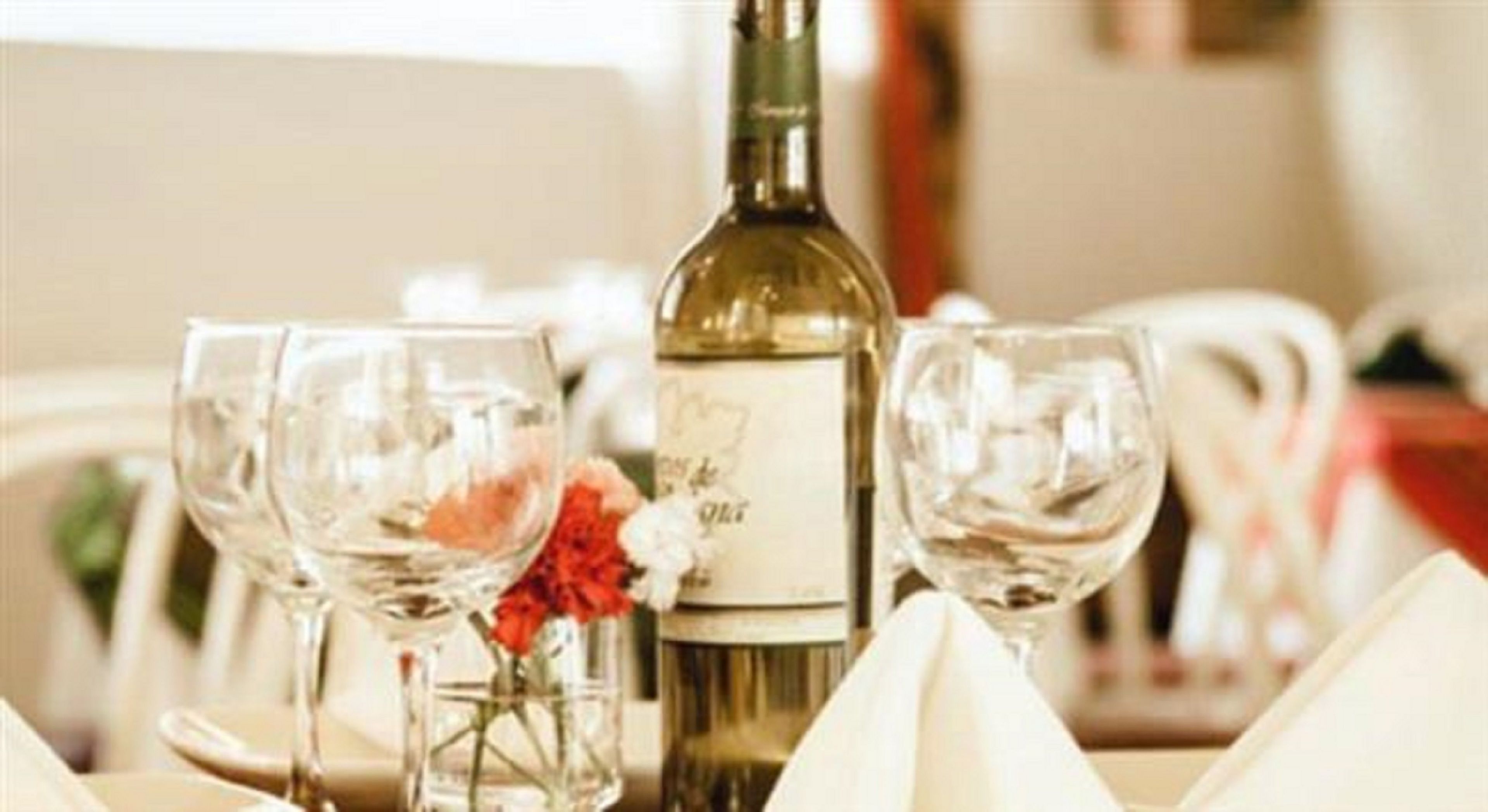 Una mesa dispuesta con copas de vino, una botella y un jarrón con flores.
