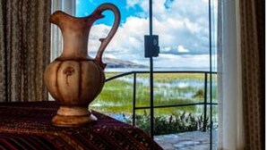 A room with a large window, a vase on a table, and a view of a landscape. - Yacht Lago Titicaca (Puno)