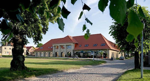 A large building with a red roof, surrounded by trees and a gravel path.