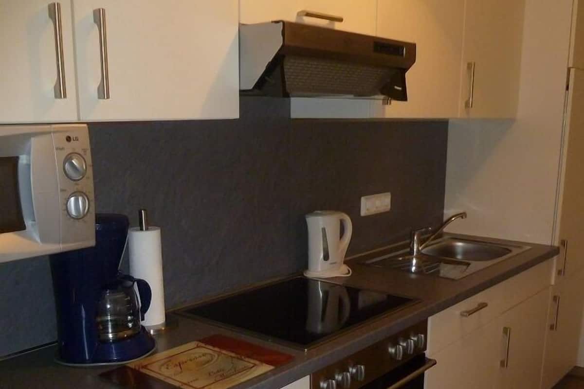 Une cuisine moderne avec des meubles blancs, un four encastré, un four à micro-ondes et une machine à café.