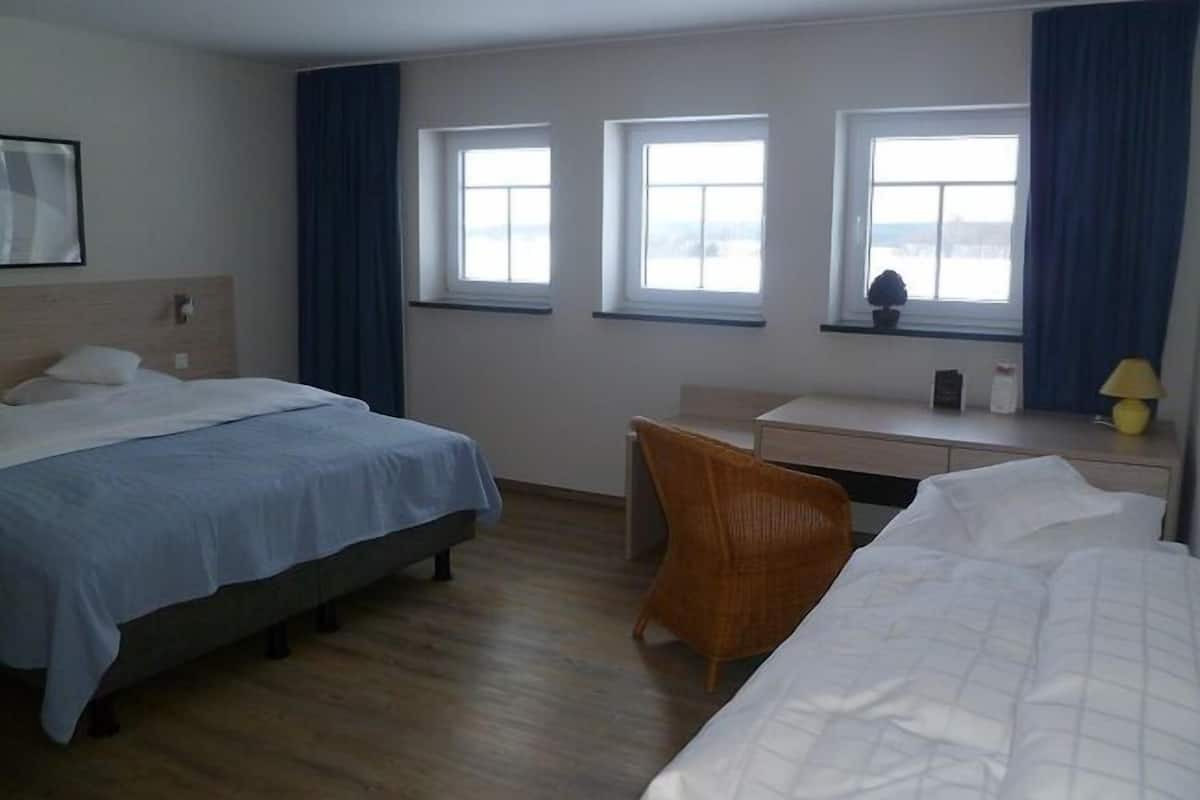 Une chambre d’hôtel avec deux lits, un bureau et trois fenêtres.