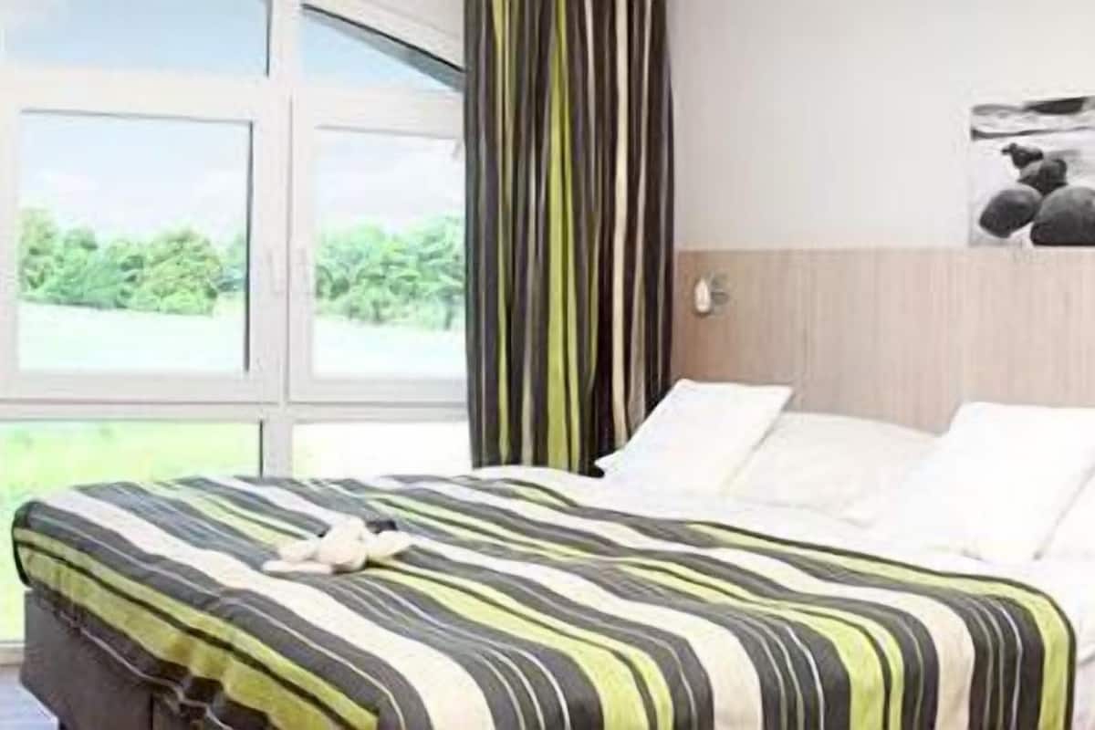 Une chambre d’hôtel équipée d’un lit, d’un bureau, d’une chaise et d’une fenêtre donnant sur un paysage verdoyant.