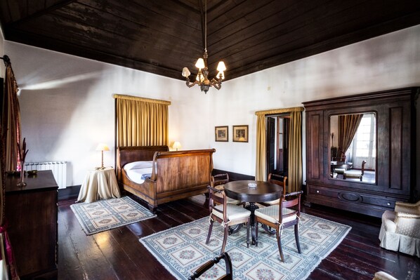 A traditional room with a wooden bed, a round table with chairs, a large mirror, and a chandelier.