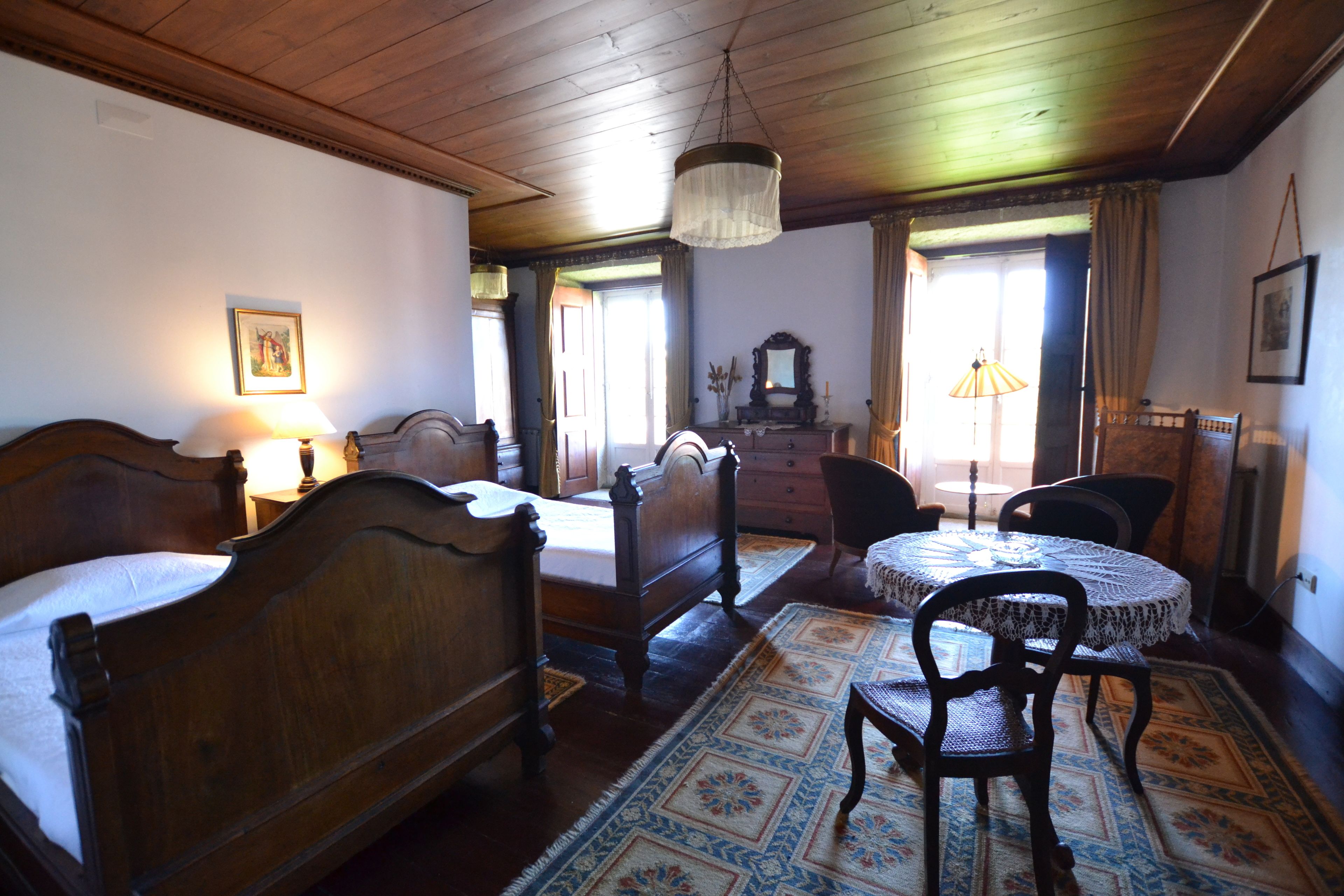 Una habitación tradicional con una cama de madera, un aparador de madera, una mesa redonda con sillas y una araña.