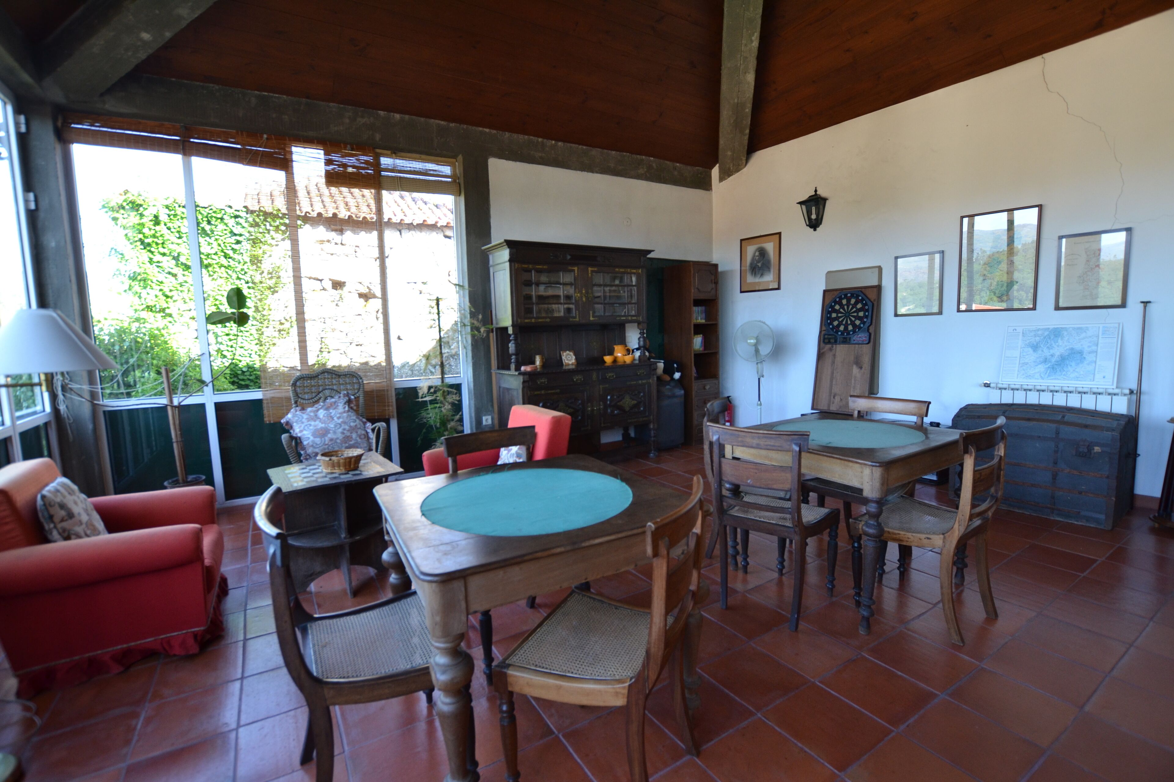 A spacious living room with a wooden dining table, red armchairs, and a large window with a view of greenery.