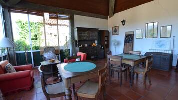 A spacious living room with a wooden dining table, red armchairs, and a large window with a view of greenery.
