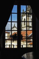 Janela com vista para um edifício com telhado de azulejos e uma cruz.