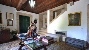Ein Zimmer mit einem Holztisch, auf dem Bücher liegen, einer grünen Tür und einer Treppe, die in eine obere Ebene führt.