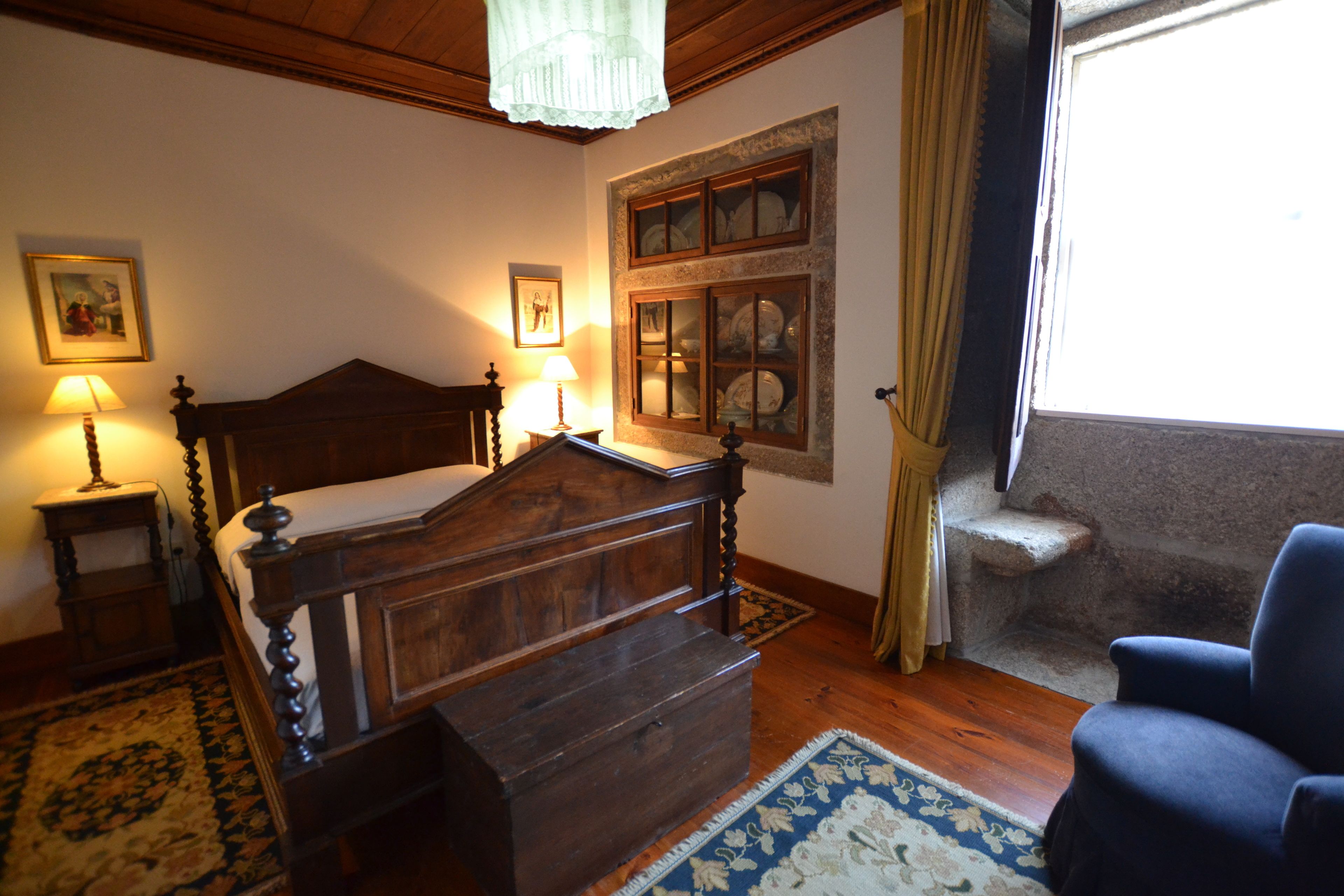 Una camera da letto con un letto a baldacchino in legno, un comodino con una lampada, una finestra vista e una poltrona blu.