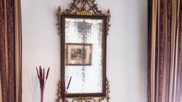 Un aparador de madera con tiradores de latón, un espejo con un marco ornamentado y dos jarrones con flores rojas.