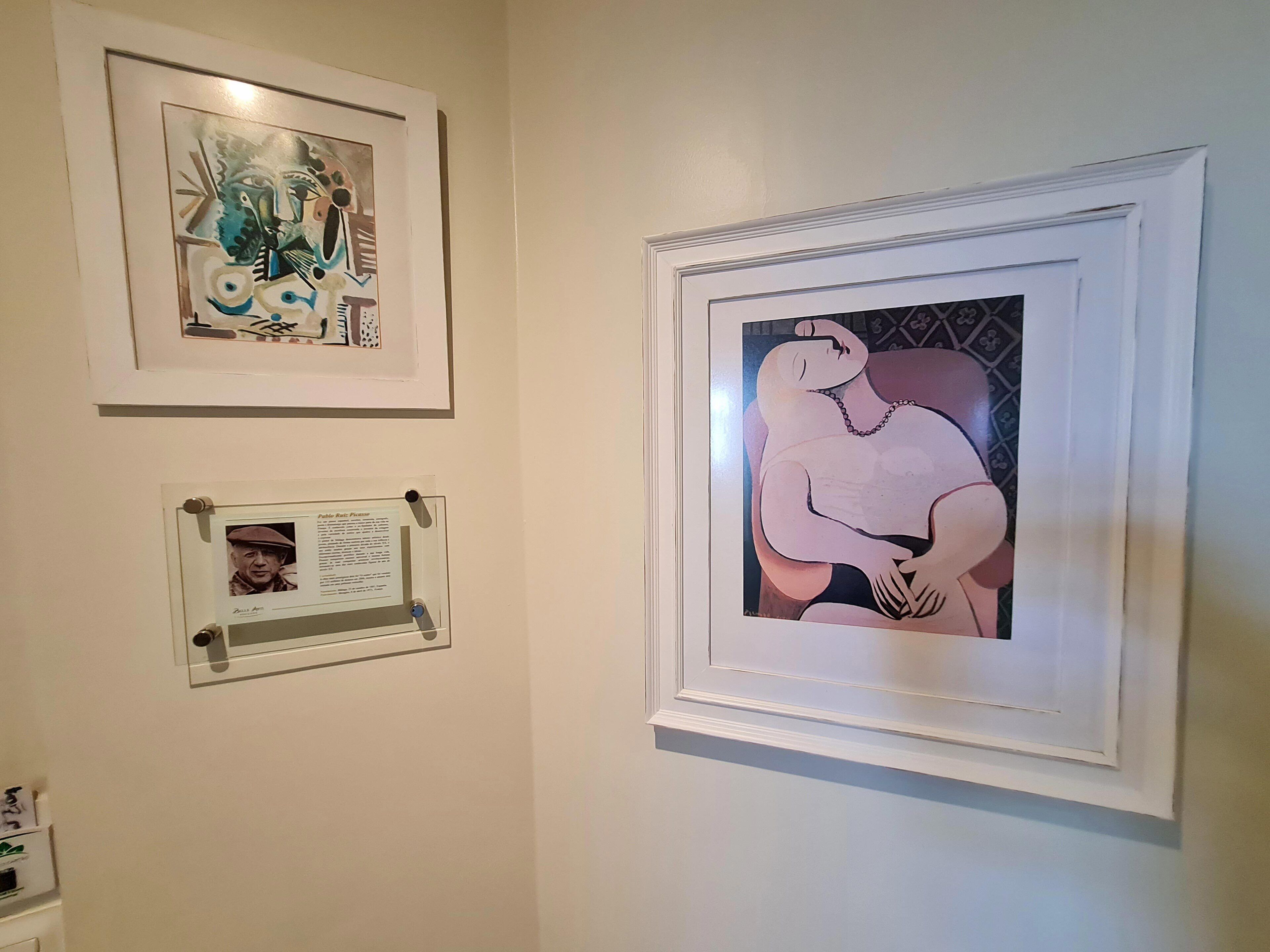 Eine Wand mit drei gerahmten Kunstwerken, darunter ein Porträt und zwei abstrakte Bilder.