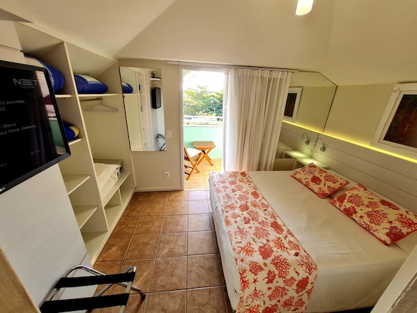 Habitación de hotel con cama, escritorio, silla, televisor y balcón con vista a zonas verdes.