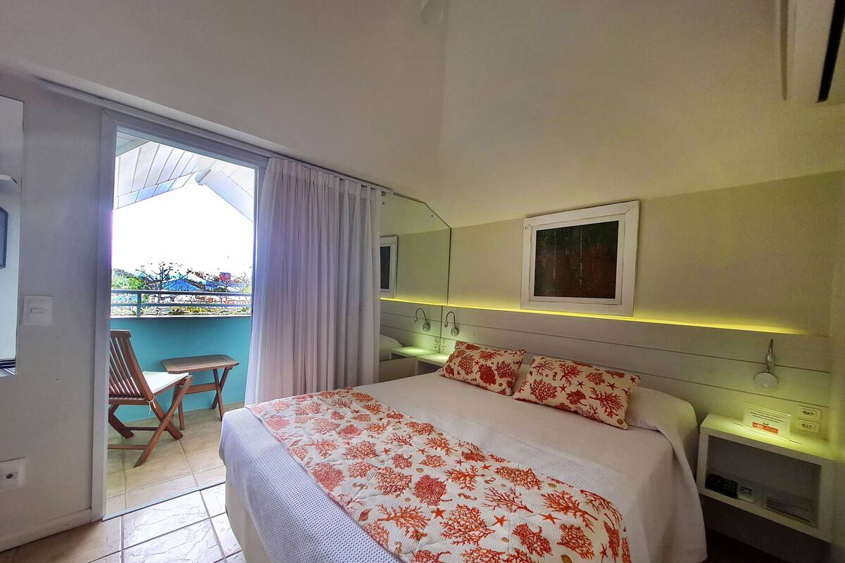 A hotel room with a bed, a bedside table, a nightstand, a window with curtains, a chair, and a view of the outside.