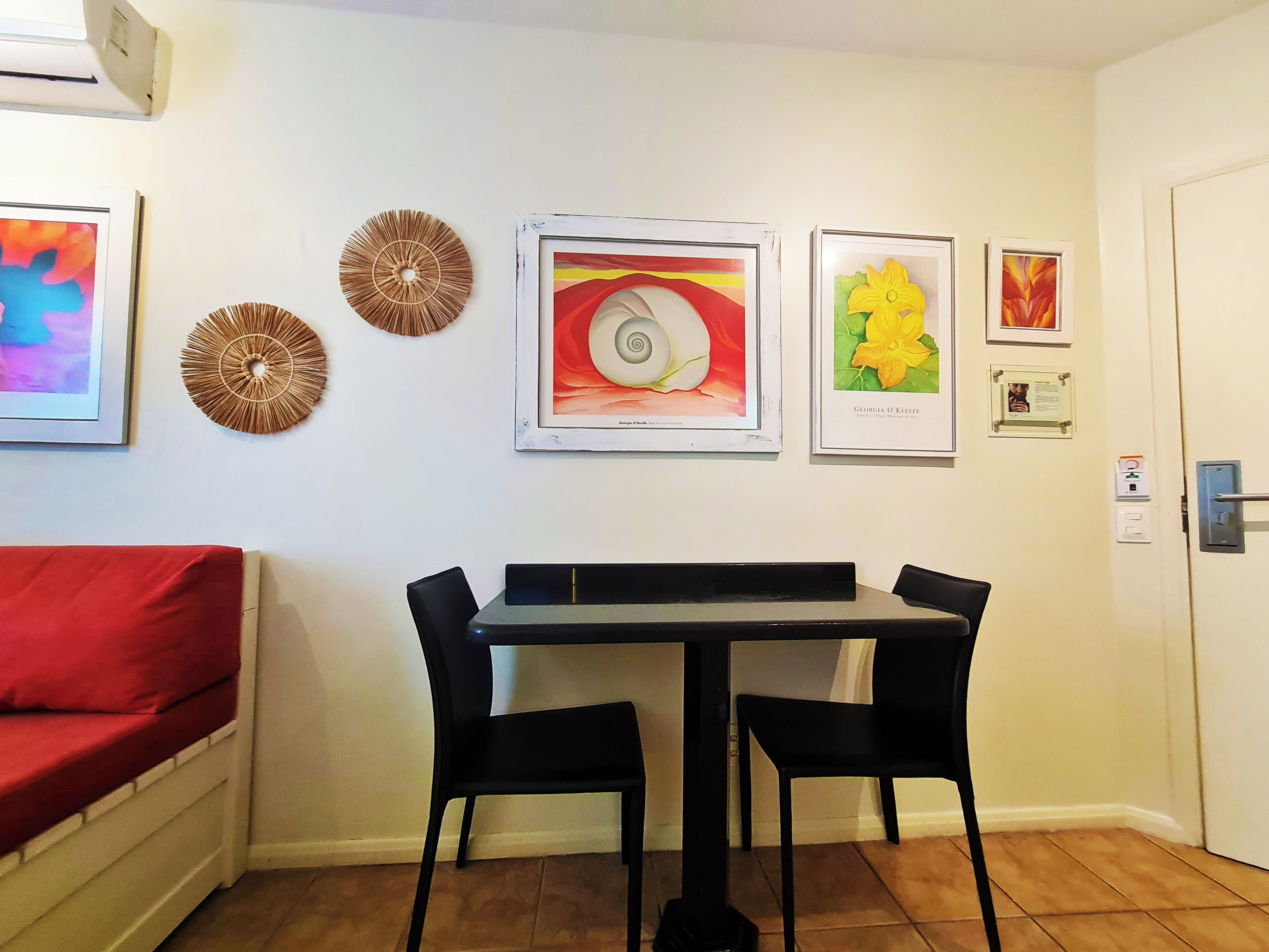 Un comedor con una mesa y sillas, un sofá rojo y obras de arte colgadas en la pared.