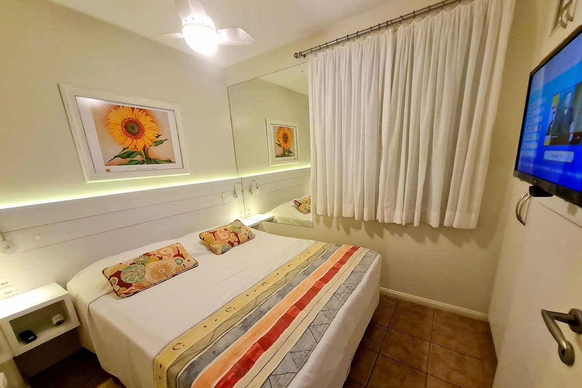 A hotel room with a bed, a nightstand, a TV, and a window with curtains.