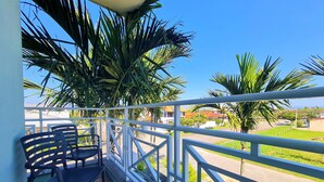 A balcony with a white railing, two black chairs, and palm trees in the background.