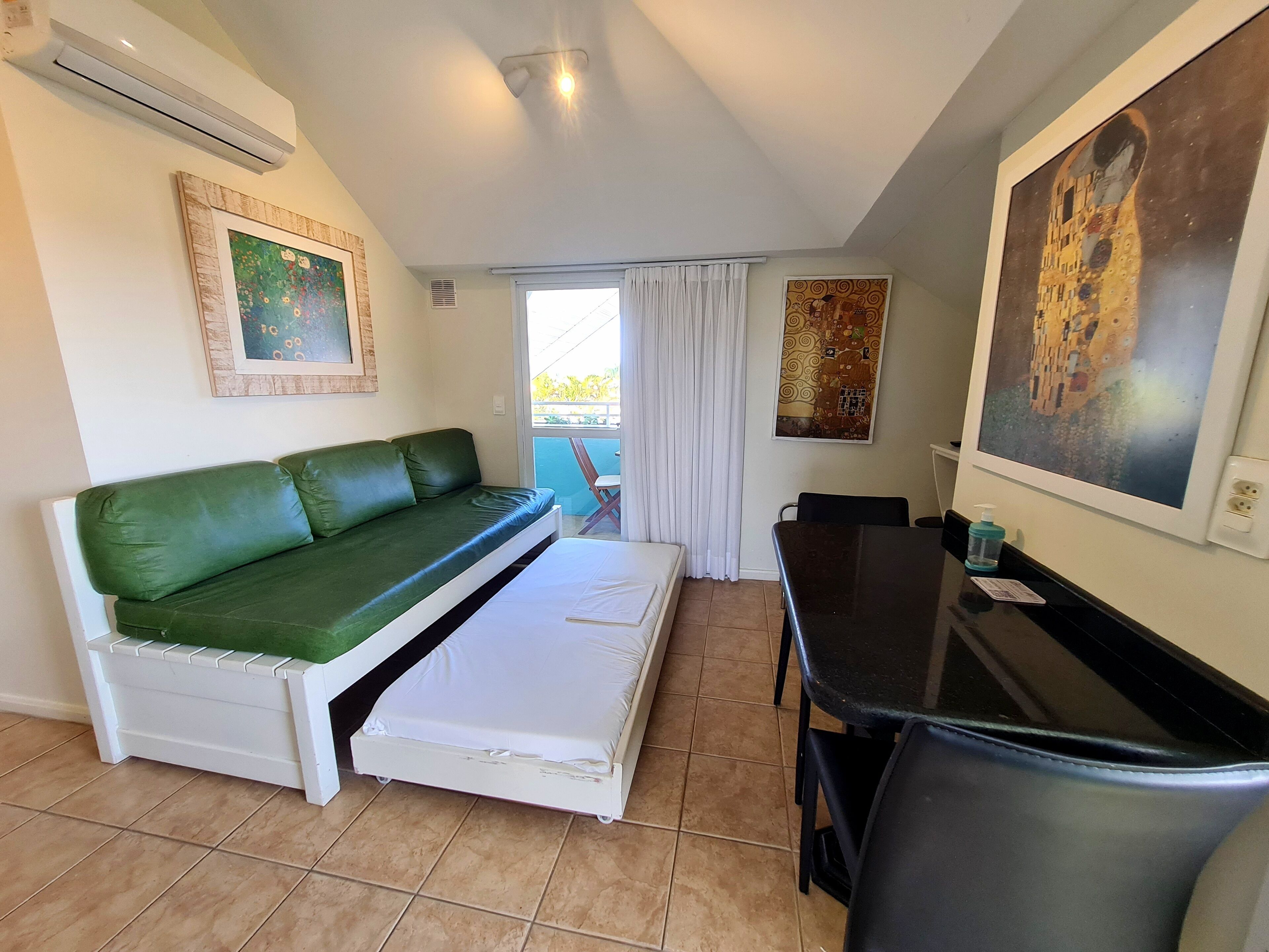 Un espacio habitable compacto con un sofá verde, una pequeña mesa de comedor y una cama blanca.