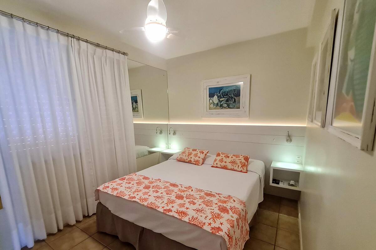 A bedroom with a bed, two bedside tables, a nightstand, a mirror, and a window with curtains.
