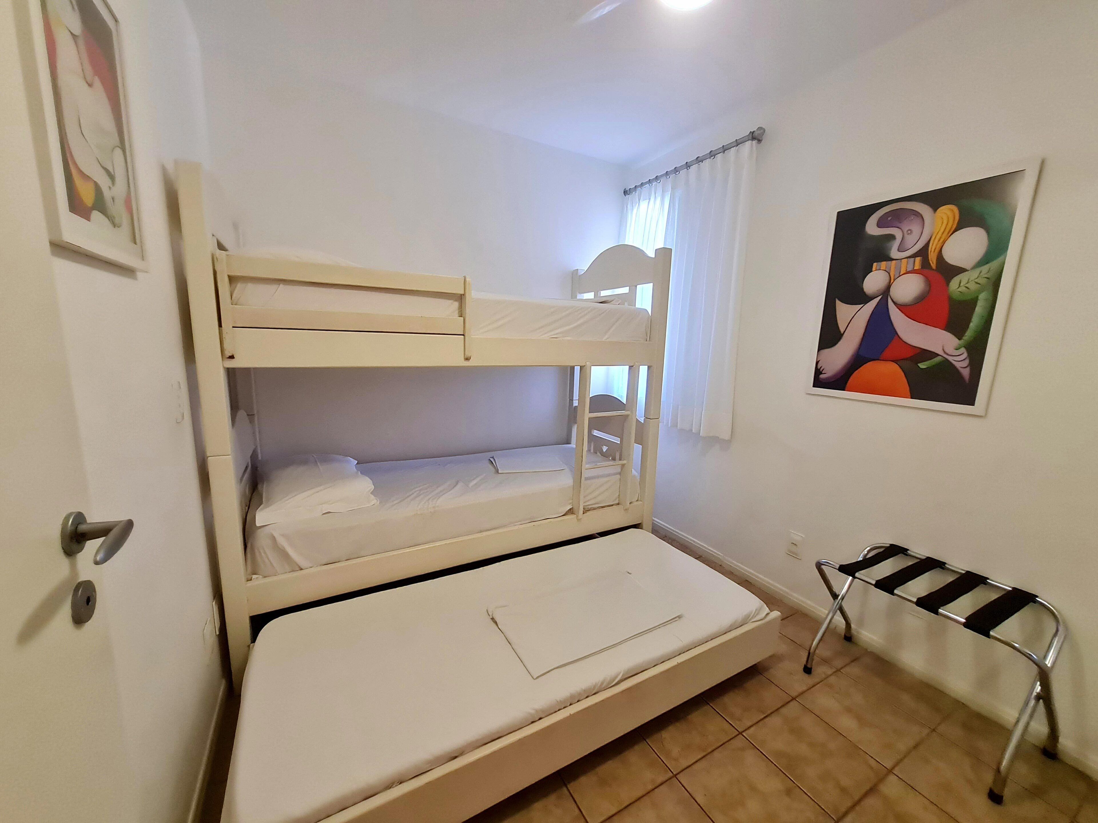 Een slaapkamer met een stapelbed, een enkel bed, een stoel, een tafeltje en een schilderij aan de muur.