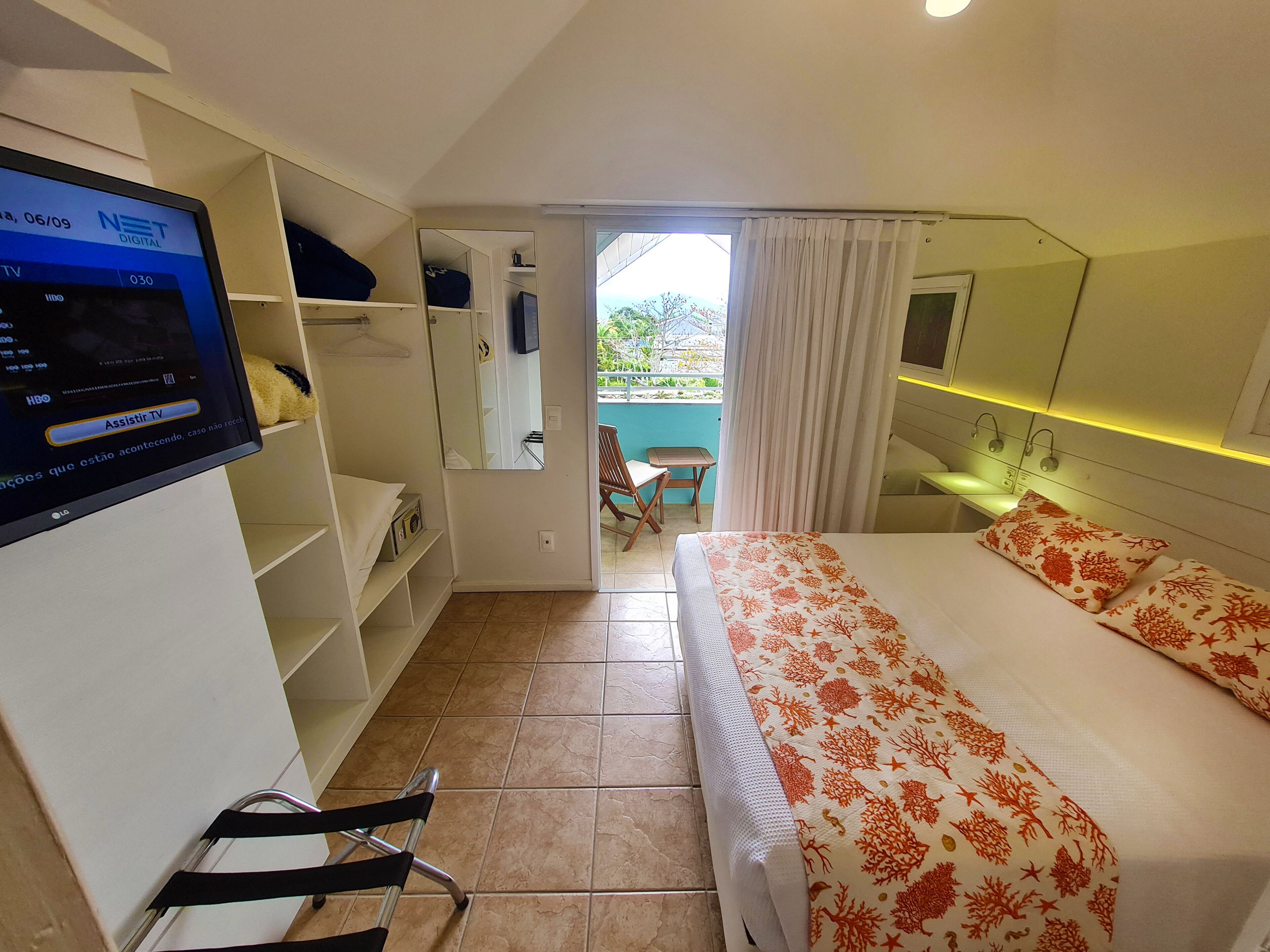 A hotel room with a bed, a TV, a wardrobe, and a small balcony.